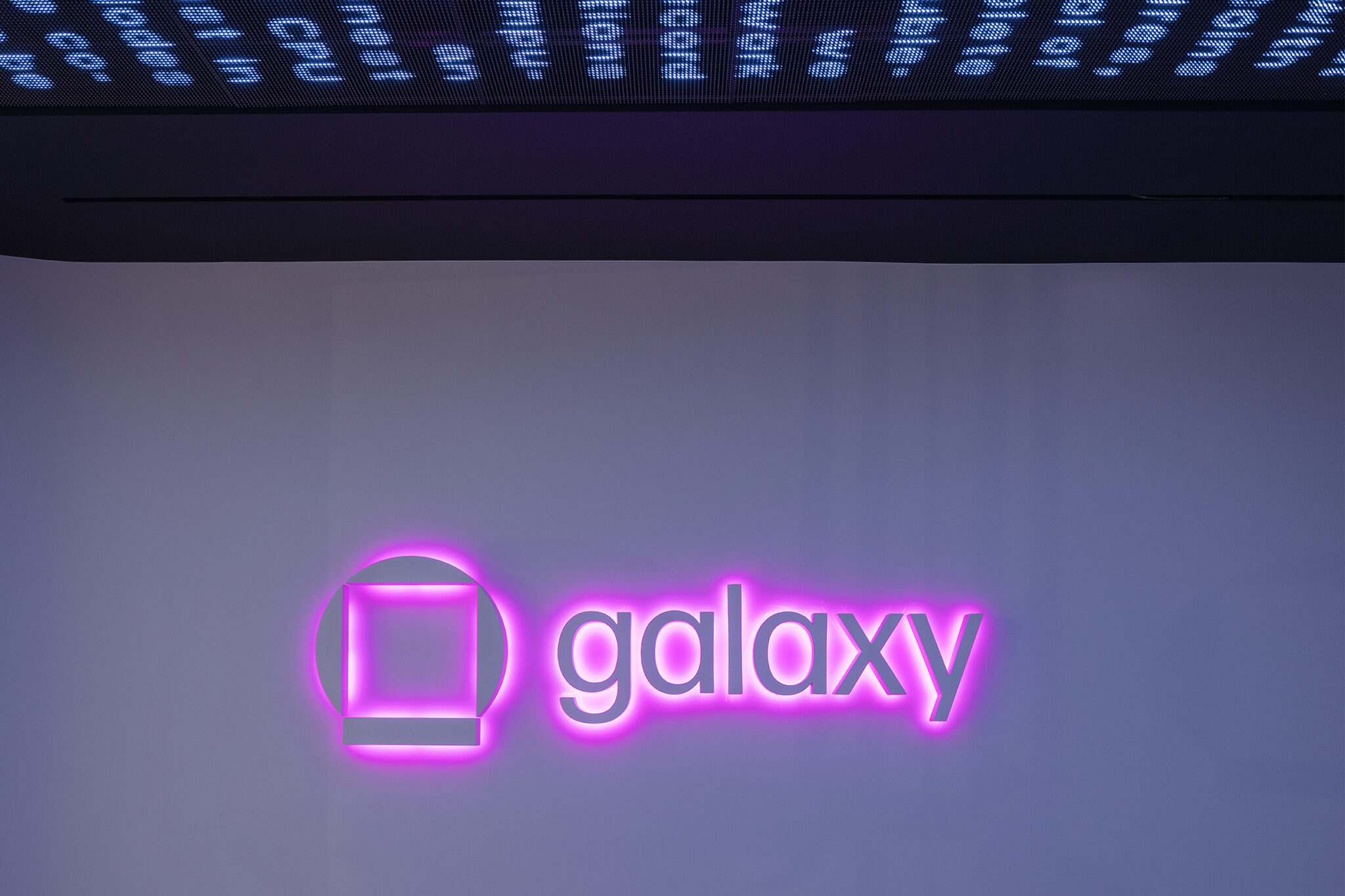 Galaxy logo sign illuminated by neon pink light glowing beneath the sign.